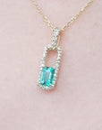 Gold necklace with a natural emerald pendant on a pink skin background.
