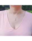 Person wearing a pink top with a necklace featuring a natural colombian emerald pendant in outdoors.
