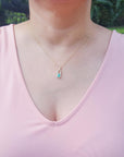 Person wearing a pink top with a necklace featuring a natural colombian emerald pendant in outdoors.