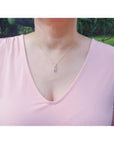 Emerald-cut emerald and diamond halo pendant on an 18K yellow gold chain, worn on a model.