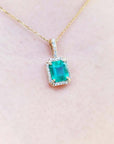 Natural colombian emerald pendant on a gold chain against a light pink skin background.