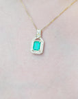 Gold necklace with a pendant featuring a colombian emerald on a light pink background