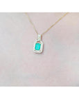Gold necklace with a pendant featuring a colombian emerald on a light pink background