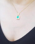 Gold necklace with an emerald-cut emerald pendant on a person wearing a black top.