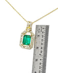 Gold necklace with an emerald pendant next to a ruler for scale on a white background