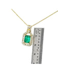 Gold necklace with an emerald pendant next to a ruler for scale on a white background