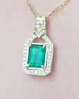 Natural colombian emerald pendant with diamond accents on a gold chain against a pink skin background