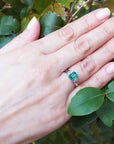 Hand wearing an emerald platinum ring with a leafy background.