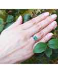 Hand wearing an emerald platinum ring with a leafy background.