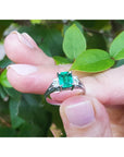 Natural emerald platinum ring held between fingers with a green leafy background