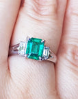 Emerald and side diamonds platinum ring on a hand.