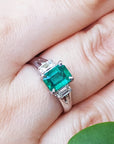 Genuine Colombian emerald platinum ring on a hand with a green leaf in the background.