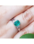 Genuine Colombian emerald platinum ring on a hand with a green leaf in the background.