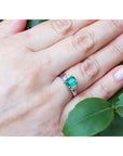 Hand wearing a brides emerald platinum ring with a leafy background.