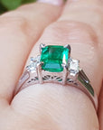Emerald-cut emerald platinum ring held on a hand.