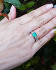 Hand wearing a natural Colombian emerald ring on a green leafy background.
