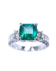 A real colombian emerald ring with side princess cut diamonds on front position displaying top and sideways band profile.