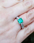 A woman's hand wearing an emerald and princess cut diamond engagement ring.