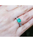 A woman's hand wearing an emerald and princess cut diamond engagement ring.