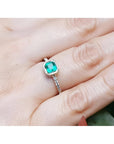 14K yellow gold ring with a bezel-set emerald and accent diamonds on a woman's finger.
