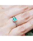 14K yellow gold ring with a bezel-set emerald and accent diamonds on a woman's finger.