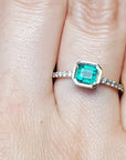 A bezel set natural colombian emerald ring with accent diamonds on a finger.