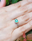 Hand wearing a bezel emerald set ring accent diamonds against a natural background.
