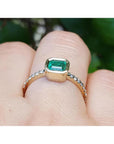 Bezel-set emerald ring with accent diamonds in 14K yellow gold, worn on a finger.
