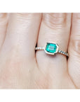 A bezel set natural colombian emerald ring with accent diamonds on a finger.