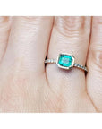 A bezel set natural colombian emerald ring with accent diamonds on a finger.