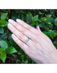 Hand wearing a 14K yellow gold east-west emerald-cut bezel set ring with accent diamonds.