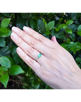 Hand wearing a 14K yellow gold east-west emerald-cut bezel set ring with accent diamonds.