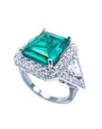 18K white gold ring with a rectangular emerald, diamond halo, and trillion side diamonds.