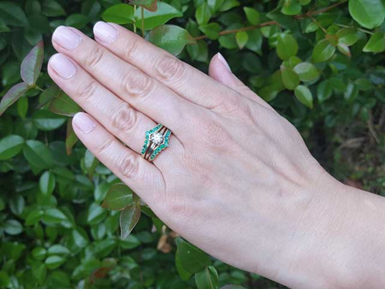 Hand wearing a ring guard with a solitaire diamond ring against a green leafy background.