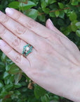 Hand wearing a ring guard with a solitaire diamond ring against a green leafy background.