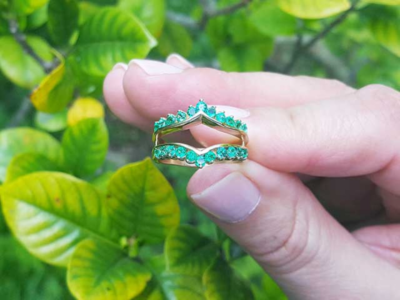 Hand wearing an emerald ring guard with a green leafy background.