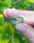 Hand wearing an emerald ring guard with a green leafy background.