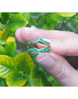 14K yellow gold emerald ring guard with 0.75 ct. round-cut Colombian emeralds, held against green leaves.