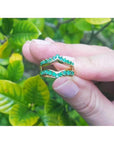 14K yellow gold emerald ring guard with 0.75 ct. round-cut Colombian emeralds, held against green leaves.