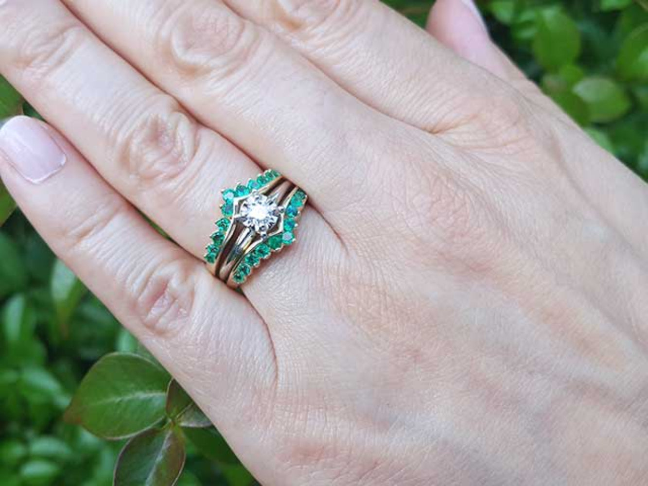 Hand wearing a ring guard with an inserted solitaire diamond ring against a blurred green background.