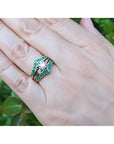Hand wearing a 14K yellow gold emerald ring guard with a solitaire diamond ring, surrounded by green leaves.