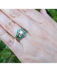 Hand wearing a 14K yellow gold emerald ring guard with a solitaire diamond ring, surrounded by green leaves.