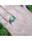 Hand wearing a 14K yellow gold emerald ring guard with a solitaire diamond ring, surrounded by green leaves.