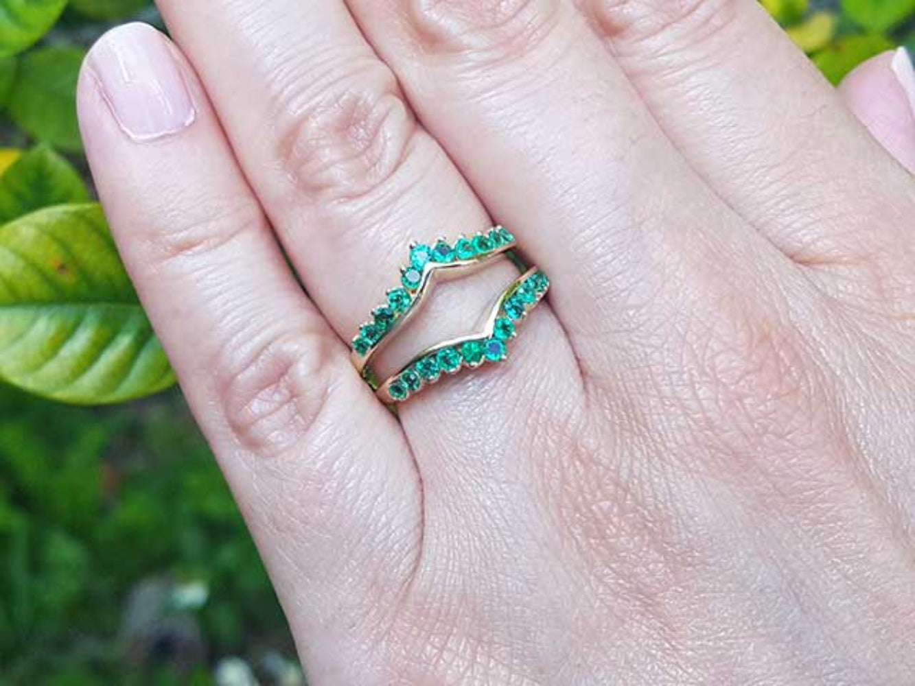 Hand wearing a yellow gold ring guard against a blurred green background.