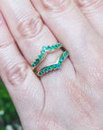 Hand wearing a yellow gold ring guard against a blurred green background.