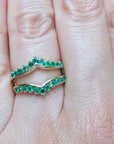 An emerald ring guard on a finger with a blurred green background.