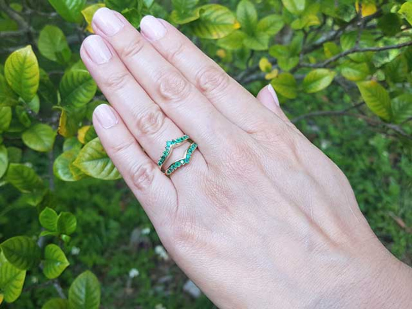 Hand wearing an emerald ring guard with a blurred green leafy background.