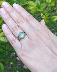 Hand wearing an emerald ring guard with a blurred green leafy background.