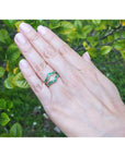 Hand wearing an emerald ring guard with a blurred green leafy background.