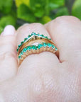 A yellow gold emerald ring guard on a hand against a blurred green leafy background,